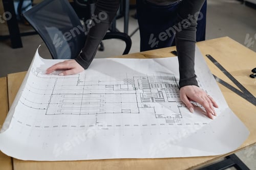 Preview: Young Adult Caucasian Woman Reviewing Architectural Blueprint on Desk