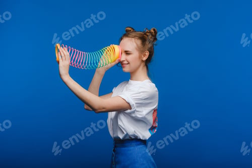 Preview: Beautiful young girl playing with a rainbow slinky, a toy of her childhood on a blue background