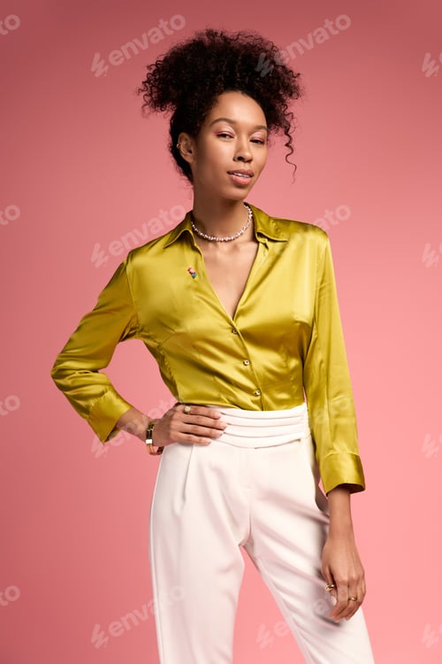 Preview: Beautiful young woman in stylish attire poses confidently against a soft pink background