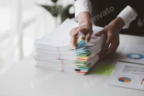 Preview: Businessman looking through stacks of papers on desk, corporate financial papers.