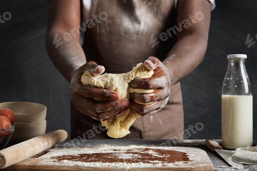 Preview: Cropped shot of hard working male cook stands in kitchen space, kneads thoroughly pastry, going to b