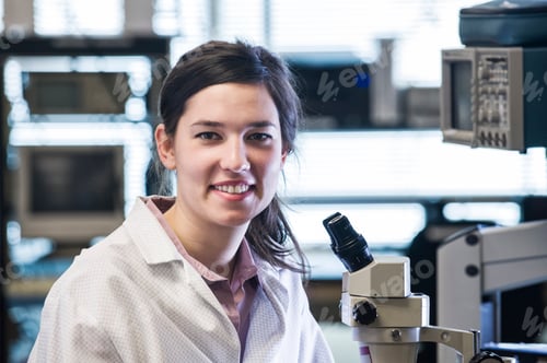 Preview: A portrait of a female techniciain at a microscope in a technical research and development site.
