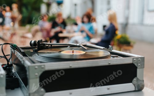 Preview: Street music festival, close-up of vinyl turntable and people sitting in cafe in bokeh.