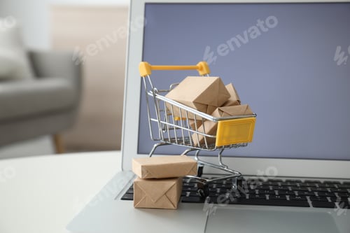 Preview: Internet shopping. Laptop and small cart with boxes on table indoors