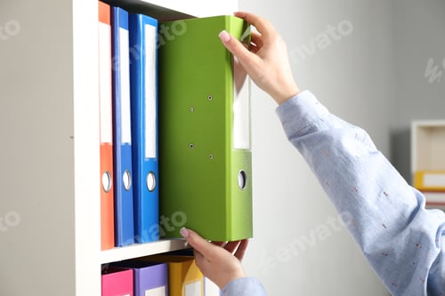 Preview: Woman taking binder office folder from shelving unit indoors, closeup