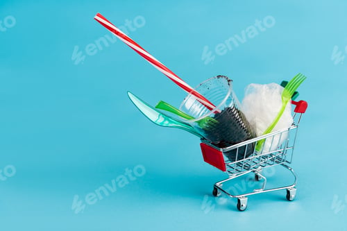 Preview: disposable plastic objects and ground in small shopping cart on blue background