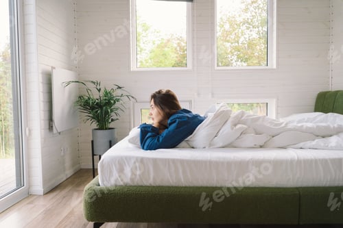 Preview: Joyful woman relaxing on soft white bed linen in a cozy bedroom during morning hours