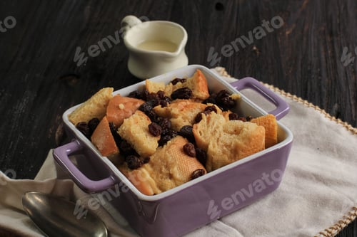 Preview: Close Up Cinnamon Bread and Butter Pudding with Raisins in Clear Baking Dish, Served with Vla