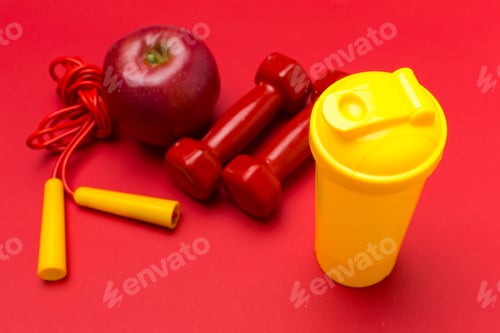 Preview: Bright workout essentials including weights, apple, and water bottle on a red background