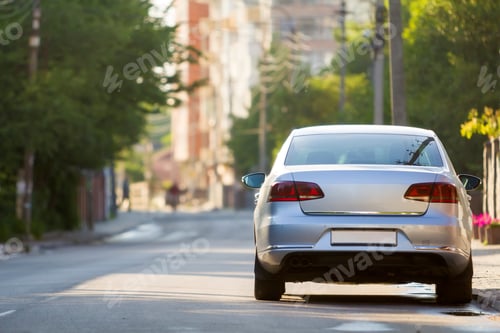 Preview: Close-up back view of new shiny expensive silver car moving along city street on blurred trees, cars