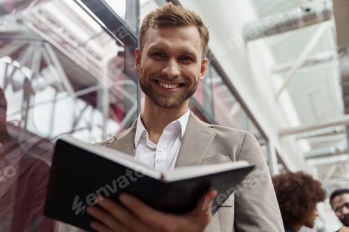 Preview: Smiling handsome businessman standing in office and looking at camera on colleagues background