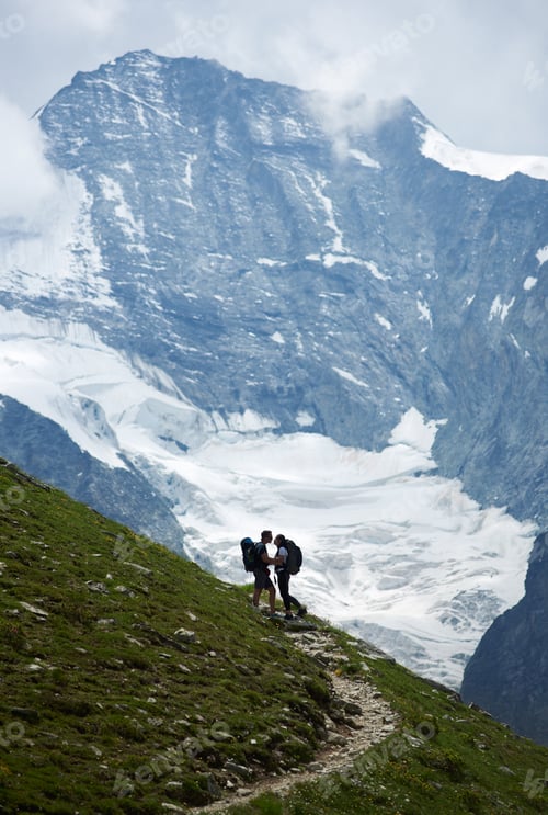 Preview: Romantic couple standing on a green meadow at rocky background of Swiss Alps