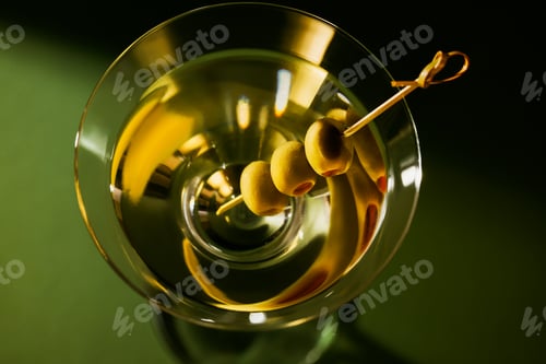 Preview: Glass of classic dry martini cocktail with olives on dark green background.