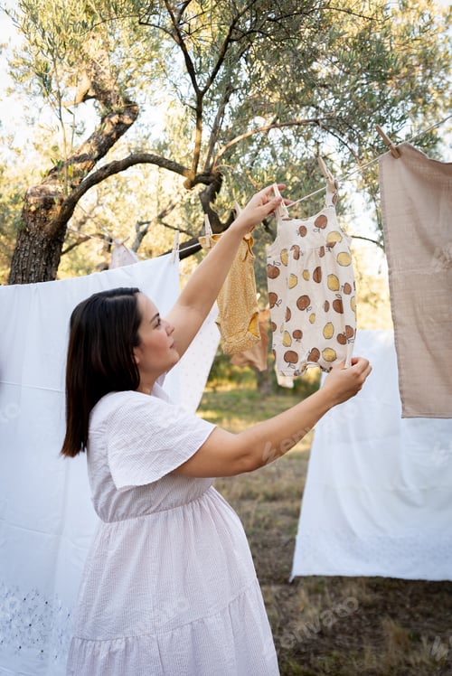 Preview: Pregnant woman hanging wash clothes on the rope for drying