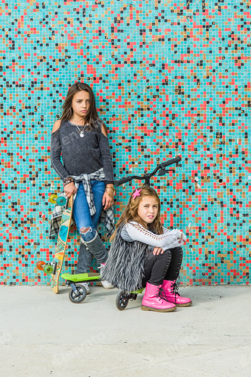 Preview: Portrait of two sisters with skateboards and scooter by multi-coloured urban wall