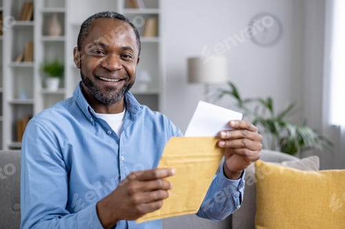 Preview: Close-up portrait of a smiling African-American man sitting at home and holding an open envelope