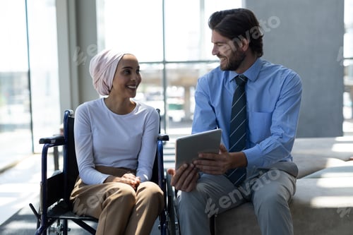 Preview: Disabled female executive with businessman discussing over digital tablet in the lobby at office