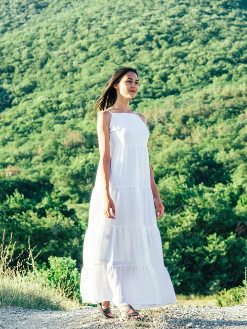 Preview: Full length of young brunette hair woman posing in summerfield in white dress. Mountain view.