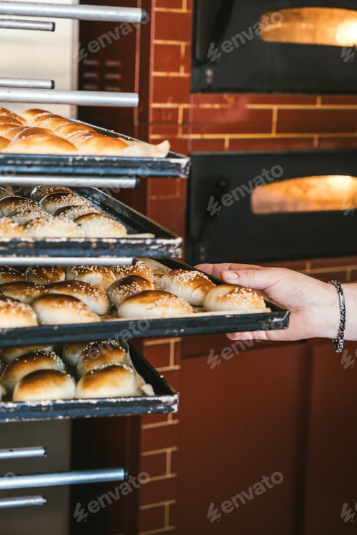 Preview: Unrecognizable baker puts bread on shelf. Fresh buns from the oven. Transportation of baking.