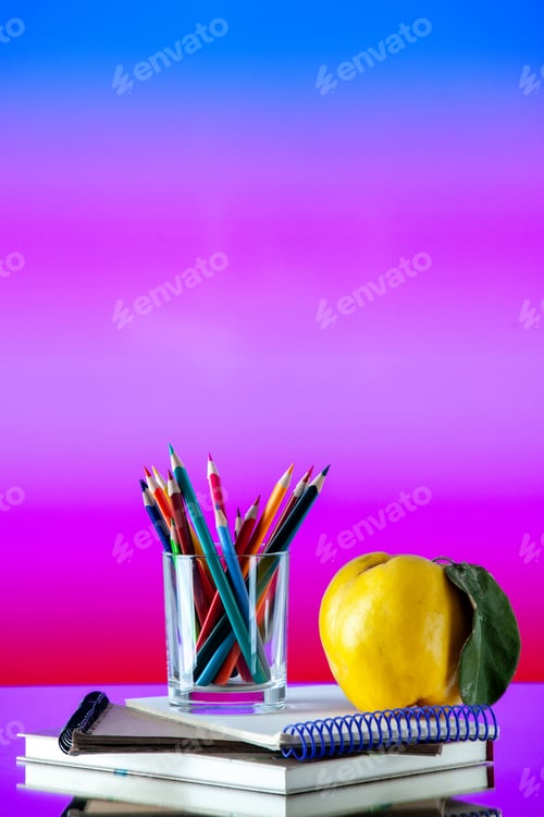 Preview: Vertical view of colored pencils kept in a glass jar and quince with stem on stacked spiral