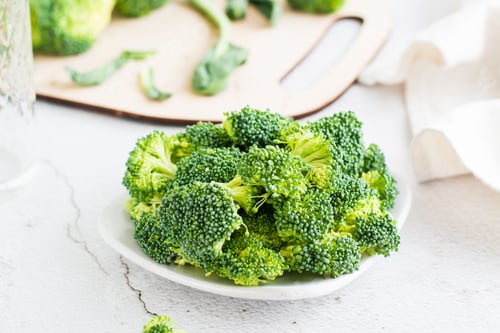 Preview: Pieces of raw broccoli on a plate on a light table. Cooking healthy vegetarian food.