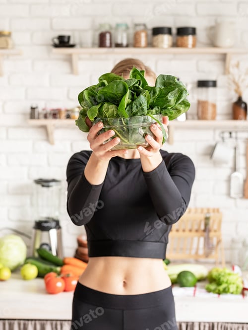 Preview: healthy eating, diet and cooking concept. Young blond smiling woman holding a bowl of fresh spinach