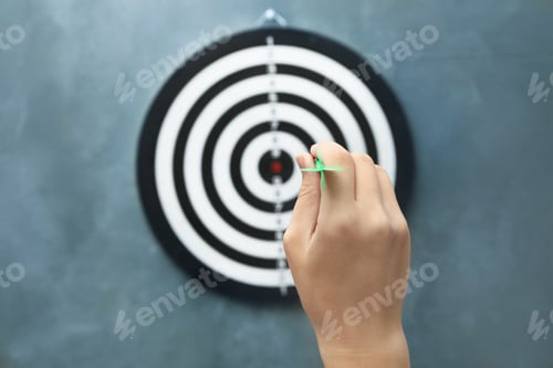 Preview: Woman throwing green arrow at dart board on grey background, closeup