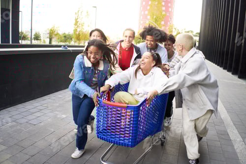 Preview: Crazy friends making a racing challenge with shopping cart. Multiracial group of young people