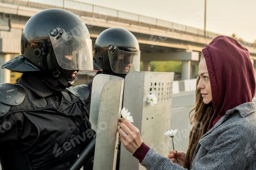 Preview: Woman attaching daisies to riot shields of police force