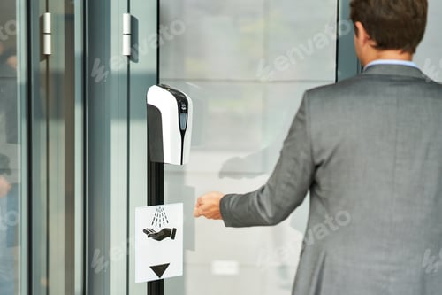 Preview: Businessman entering building using hand sanitizer due to covid-19