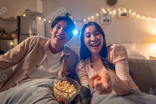 Preview: Asian young loving couple watch movie together in living room at home.