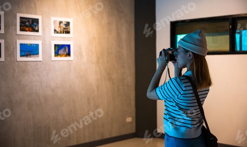Preview: Asian woman takes picture art gallery collection in front framed paintings pictures on white wall