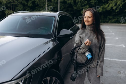 Preview: Woman With Electric Vehicle Charging Cable in Parking Lot