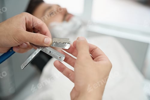 Preview: Careful barber getting ready to shave guest face with straight razor