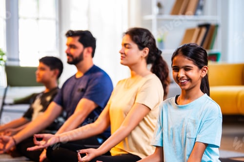 Preview: Happy Indian parents and kids practicing pranayama yoga together indoors for healthy lifestyle