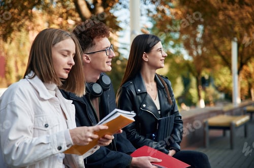 Preview: Sitting together. Three young students are outside the university outdoors