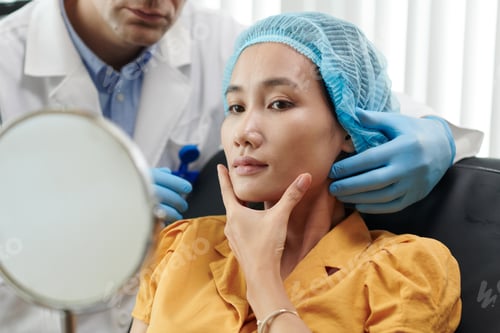 Preview: Young woman touching her face after getting beauty treatment in medical clinic