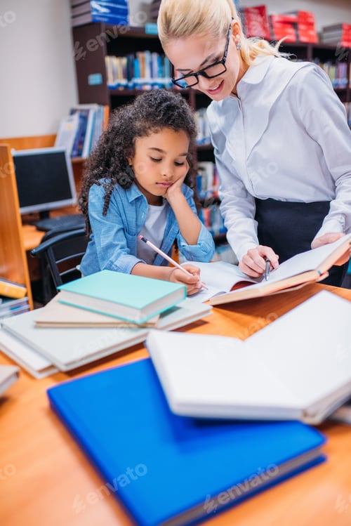 Preview: young teacher helping schoolgirl with homework in library
