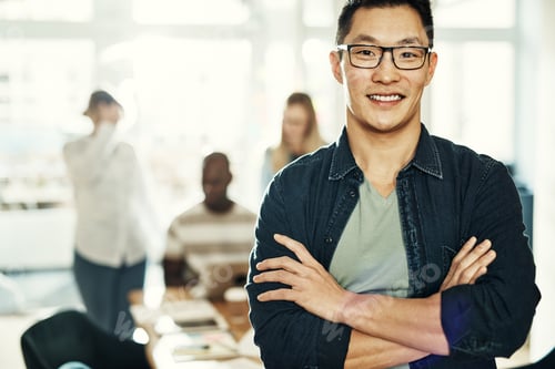 Preview: Young Asian businessman smiling with colleagues working in the background