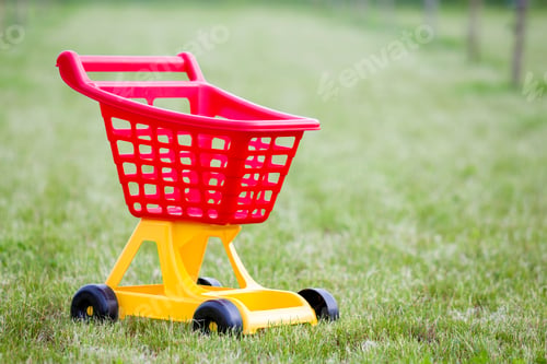 Preview: Bright plastic colorful shopping cart toy outdoors on sunny summer day.