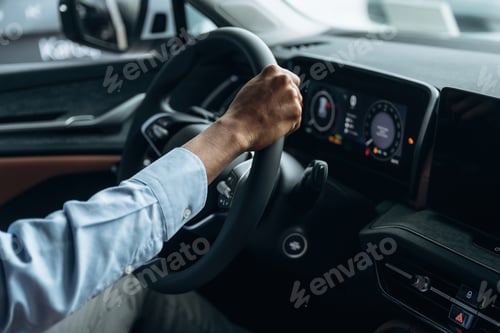 Preview: Hands are on the steering wheel. Man in shirt is in the modern car