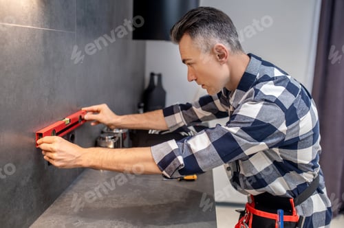 Preview: Profile of man holding level meter near wall