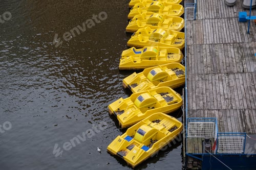 Preview: High angle shot of the yellow pedal boats tired to the wooden pier on the calm surface of the water