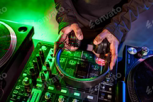 Preview: cropped view of DJ hands holding headphones over sound mixer
