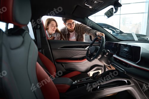 Preview: Woman with man look inside of car at dealership choosing suitable vehicle model