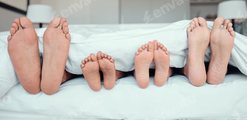 Preview: Feet of family lying in bed. Close up of feet of parents and two children in bed. Family relaxing i
