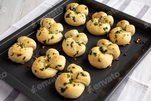 Preview: Homemade Garlic Knots with Parsley on a Baking Tray, side view.