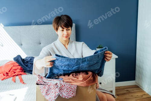 Preview: Woman selecting clothes from her wardrobe for donating to a Charity shop. Decluttering, Sorting