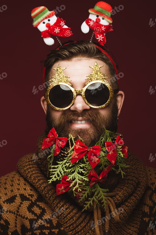 Preview: Funny bearded man in a New Year's image as Santa Claus with decorations on his beard.