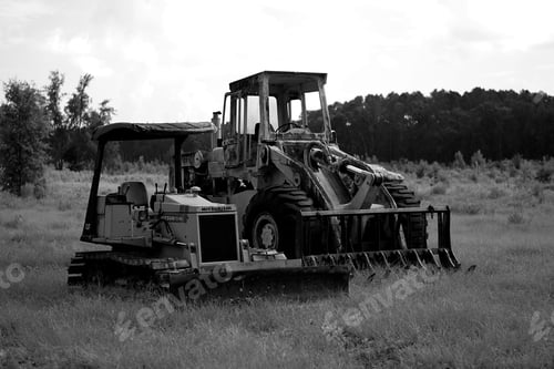 Preview: Black and white shot of a tractor on a field in a rural area in cloudy sky background